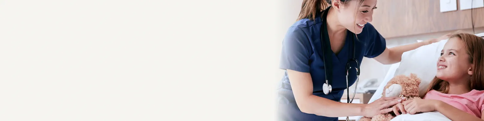 Nurse checking on a young girl and teddy bear, both in a hospital bed.
